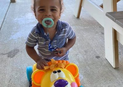 toddler smiling on lion toy with pacifer